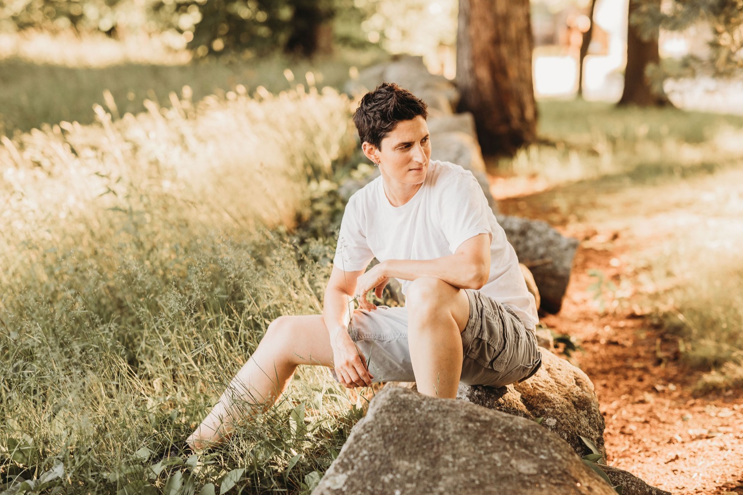 White non-binary person sitting on rock.